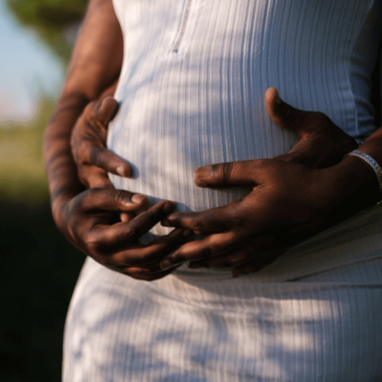 a couple holding hands over the woman’s pregnant belly