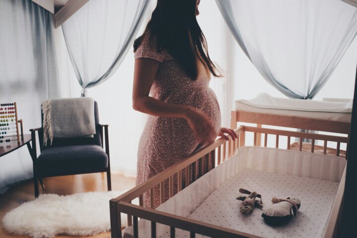 A pregnant woman in a nursery feeling guilt after a successful fertility treatment